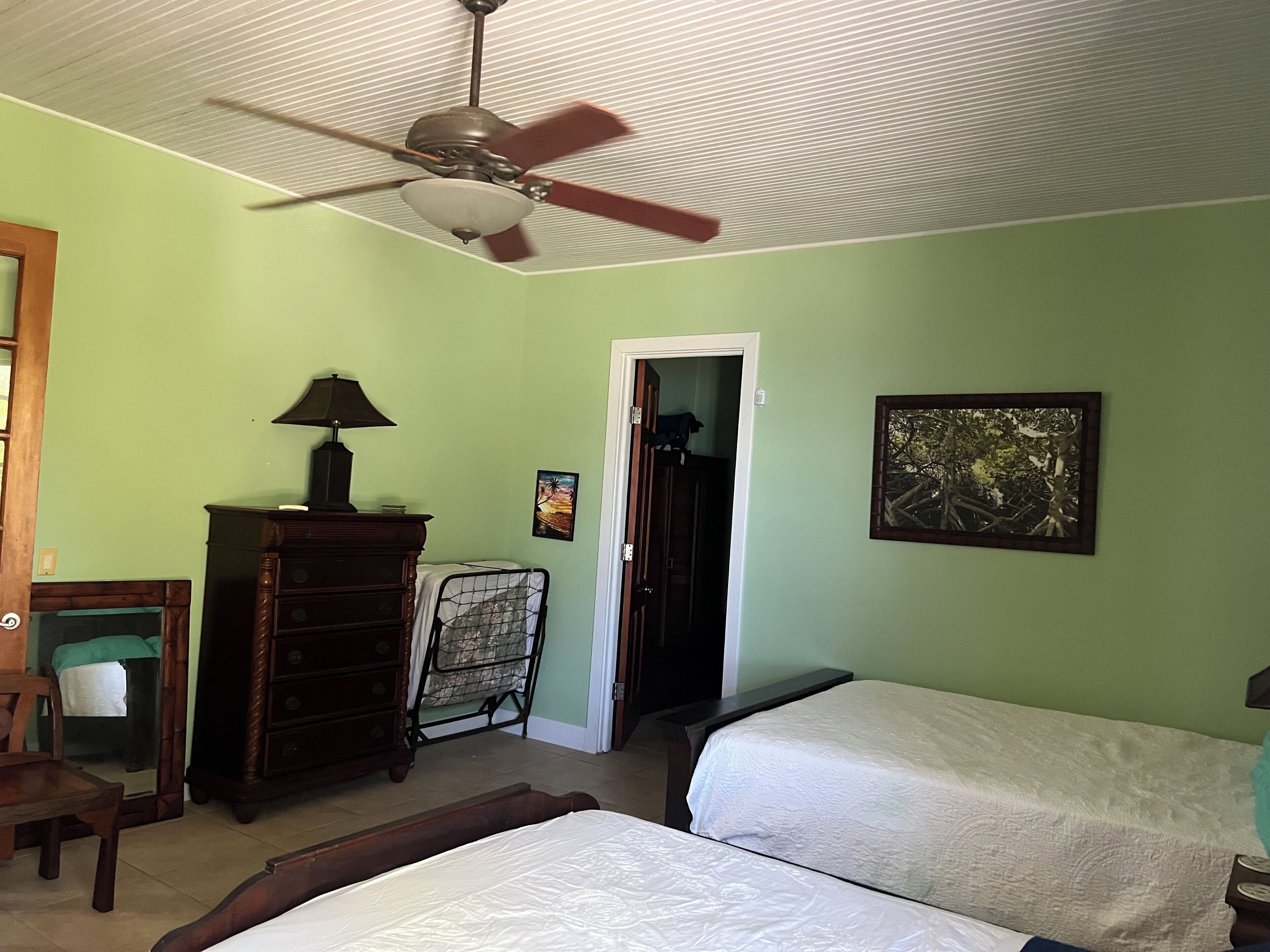 A bedroom with two beds, a ceiling fan, a dresser, a chair, and a door leading to another room.