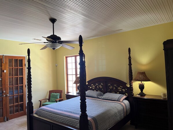 A four-poster bed with a ceiling fan, a wooden wardrobe, and a window with natural light.