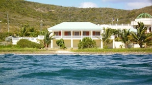Un hotel frente a la playa con fachada blanca, varios balcones y techo verde.