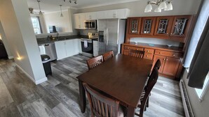Une cuisine moderne avec des meubles blancs, des appareils en acier inoxydable et une table à manger en bois.