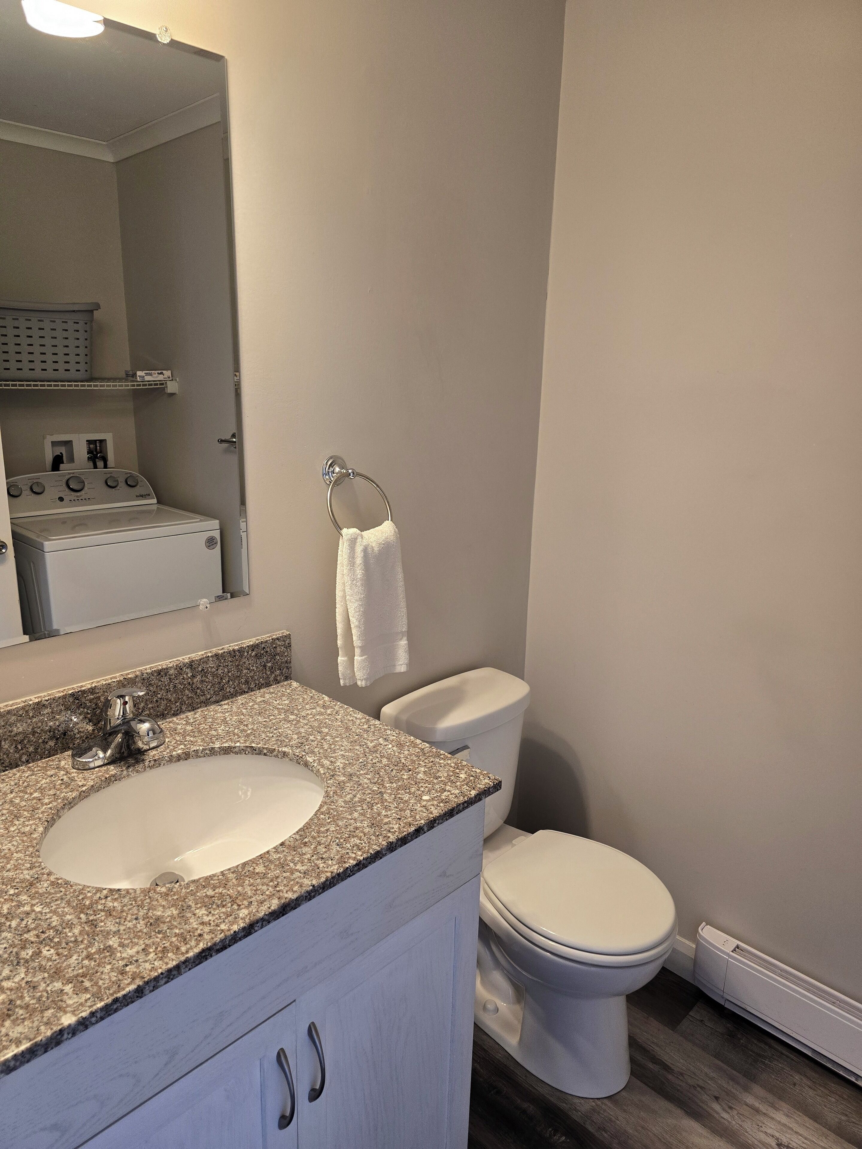 Une salle de bain avec un lavabo à dessus en granit, des toilettes blanches et une serviette accrochée au mur.