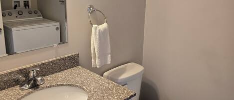 Une salle de bain avec un lavabo à dessus en granit, des toilettes blanches et une serviette accrochée au mur.