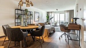 Una sala de estar moderna con una mesa de comedor de madera, asientos cómodos, una planta grande y vistas al exterior.