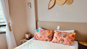 A neatly made bed with a white and orange bedspread, two decorative pillows with floral patterns, a basket with a coffee grinder and a paper, and a wall-mounted decorative item. - DM Ceara Golden Fortaleza - Beach (Meireles Fortaleza)
