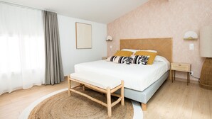 Une chambre à coucher moderne avec un grand lit, une table de chevet, un banc et une lampe fixée au mur.