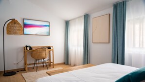 Une chambre d’hôtel moderne équipée d’un lit, d’un bureau, d’une chaise, d’une lampe et d’une grande fenêtre avec des rideaux.