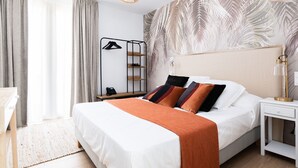 Une chambre d’hôtel bien rangée, avec un lit, une table de chevet, une lampe et un mur orné d’un motif de feuilles.