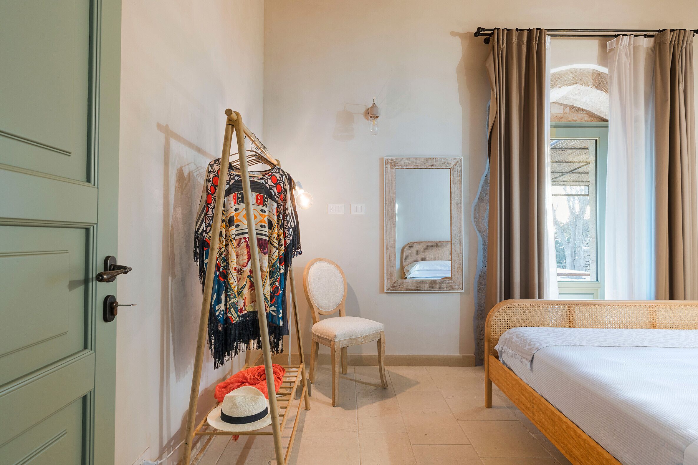 A bedroom with a bed, a chair, a clothes rack, a mirror, and a door.