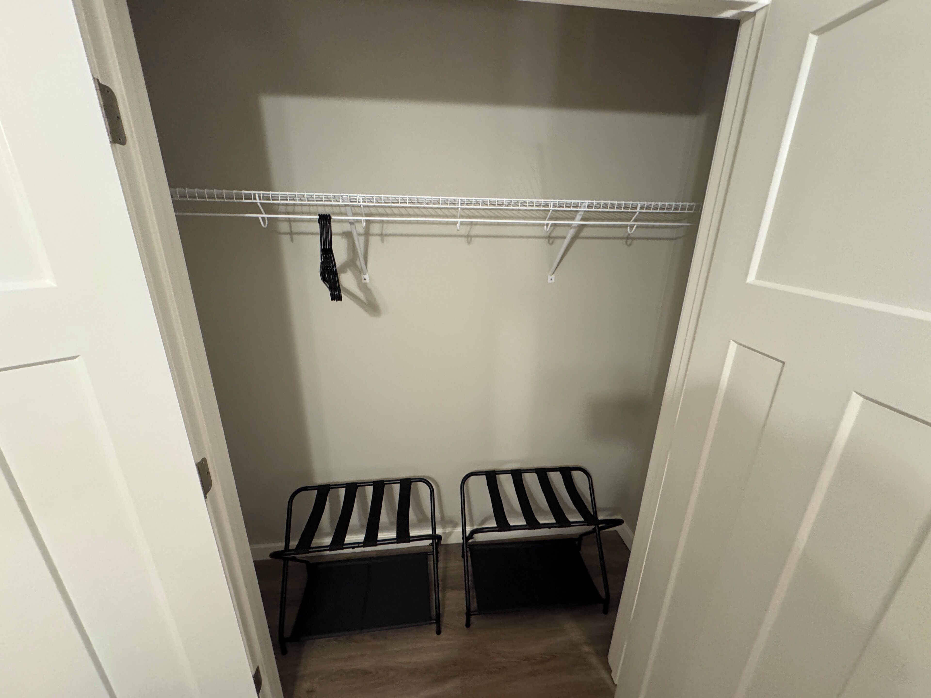 A walk-in closet with a white door, a metal shelf, and two black chairs.