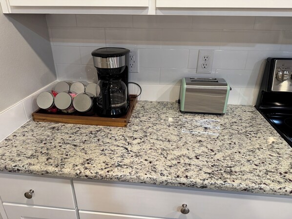 A kitchen with a granite countertop, a coffee maker, a toaster, and a wooden tray with jars.