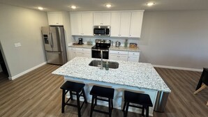 Cocina moderna con gabinetes blancos, electrodomésticos de acero inoxidable, encimera de granito y una isla central con taburetes de bar.