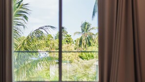 Une chambre avec un lit, une fenêtre avec des rideaux et une vue sur des palmiers et une végétation luxuriante.