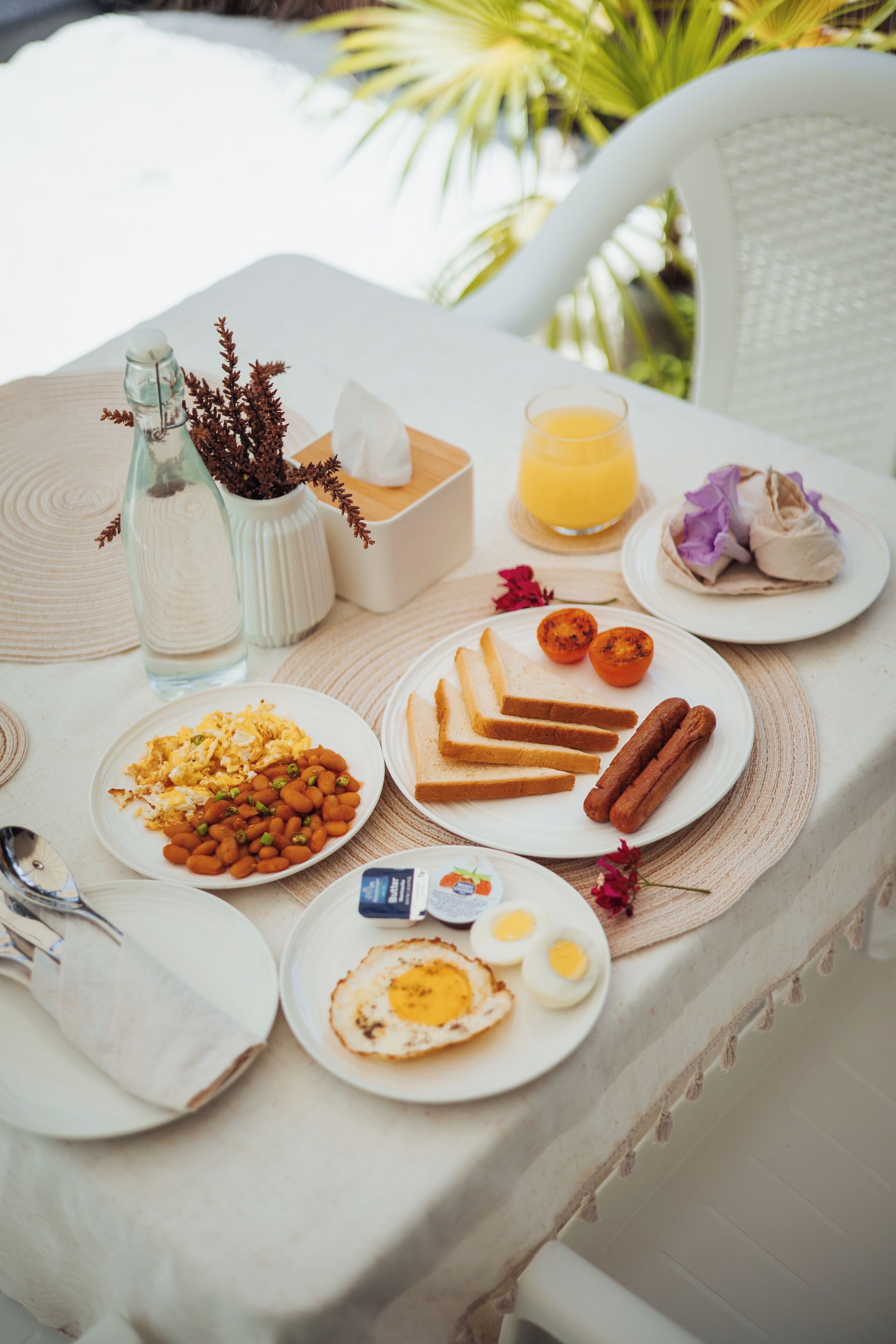 Et morgenbord med tallerkener med æg, ristet brød og pølser, en vandflaske og et glas appelsinjuice.