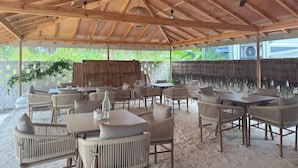Une terrasse extérieure couverte, aménagée avec des meubles en osier, des ventilateurs de plafond et des luminaires suspendus.