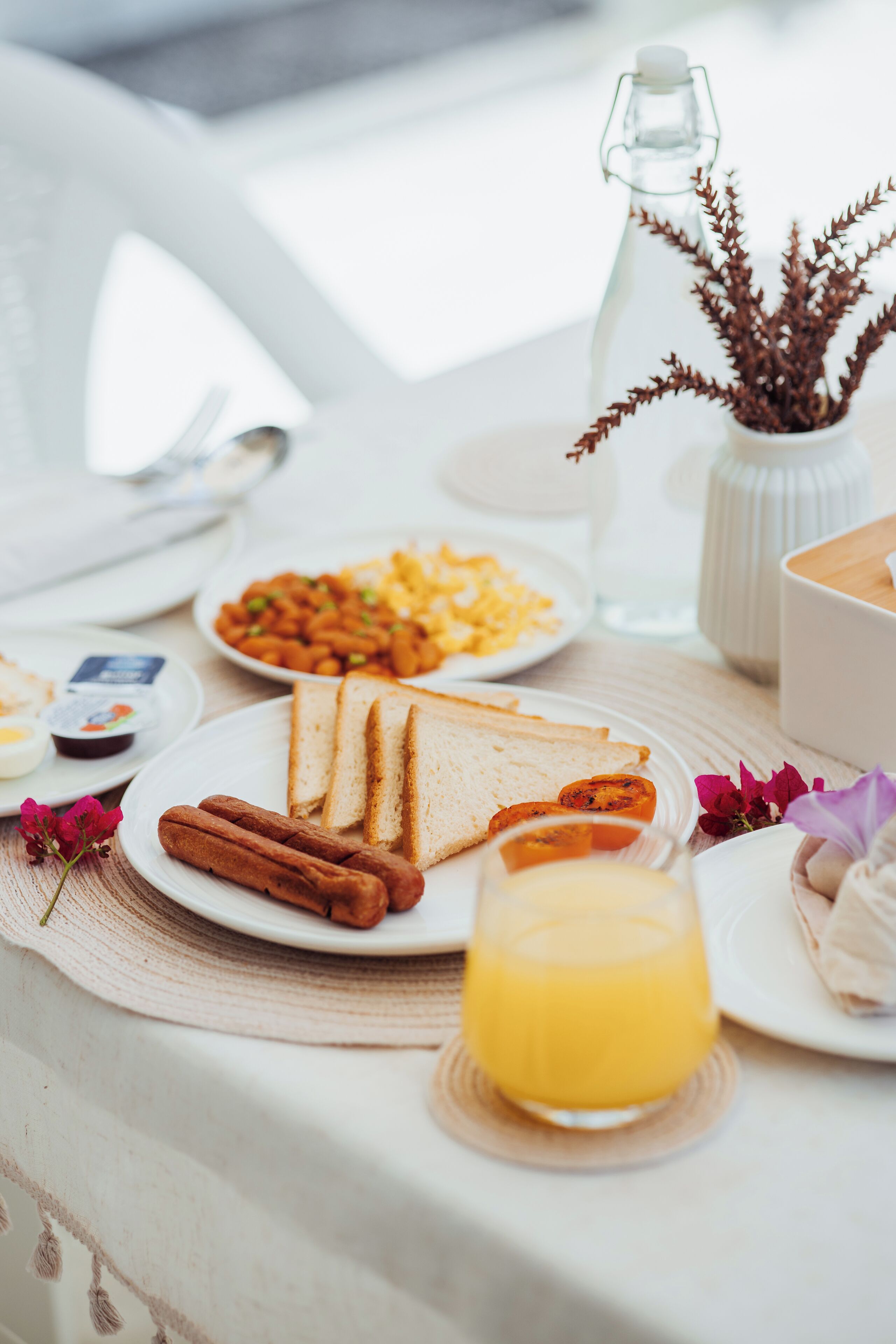 A breakfast table with plates of toast, sausages, and orange juice.