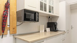 Una cocina con armarios blancos, microondas, cafetera y un paraguas rojo a cuadros colgado en la pared.