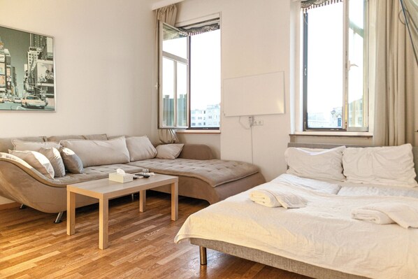 A modern hotel room with a sofa, a bed, a small table, and large windows offering a city view.