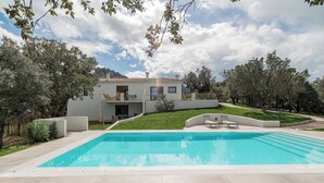 Una casa moderna de dos pisos con piscina, césped cuidado y montañas al fondo.