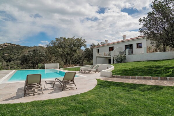 Zona de piscina con sillones reclinables y una casa con balcón.