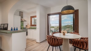 Cocina moderna con armarios blancos, una isla central y una zona de comedor con una mesa redonda y sillas tapizadas en tono café.
