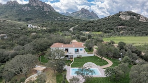 Una casa con piscina rodeada de césped cuidado y árboles, con montañas al fondo.