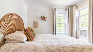 A bedroom with a large bed, a woven headboard, and a view of greenery outside. - Charming Lakeside 2-bedroom cottage in lovely Alburgh, VT (Alburgh)
