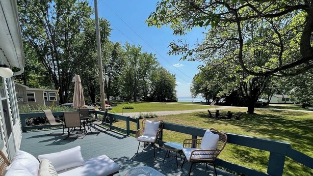 A deck with outdoor furniture, a glass table, and a view of a lake. - Charming Lakeside 2-bedroom cottage in lovely Alburgh, VT (Alburgh)