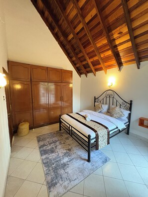 A bedroom with a bed, wooden wardrobe, and a ceiling with exposed beams. - Amora Villa, Cozy home with a beautiful lush garden, swimming pool, fitness gym. (Arusha)
