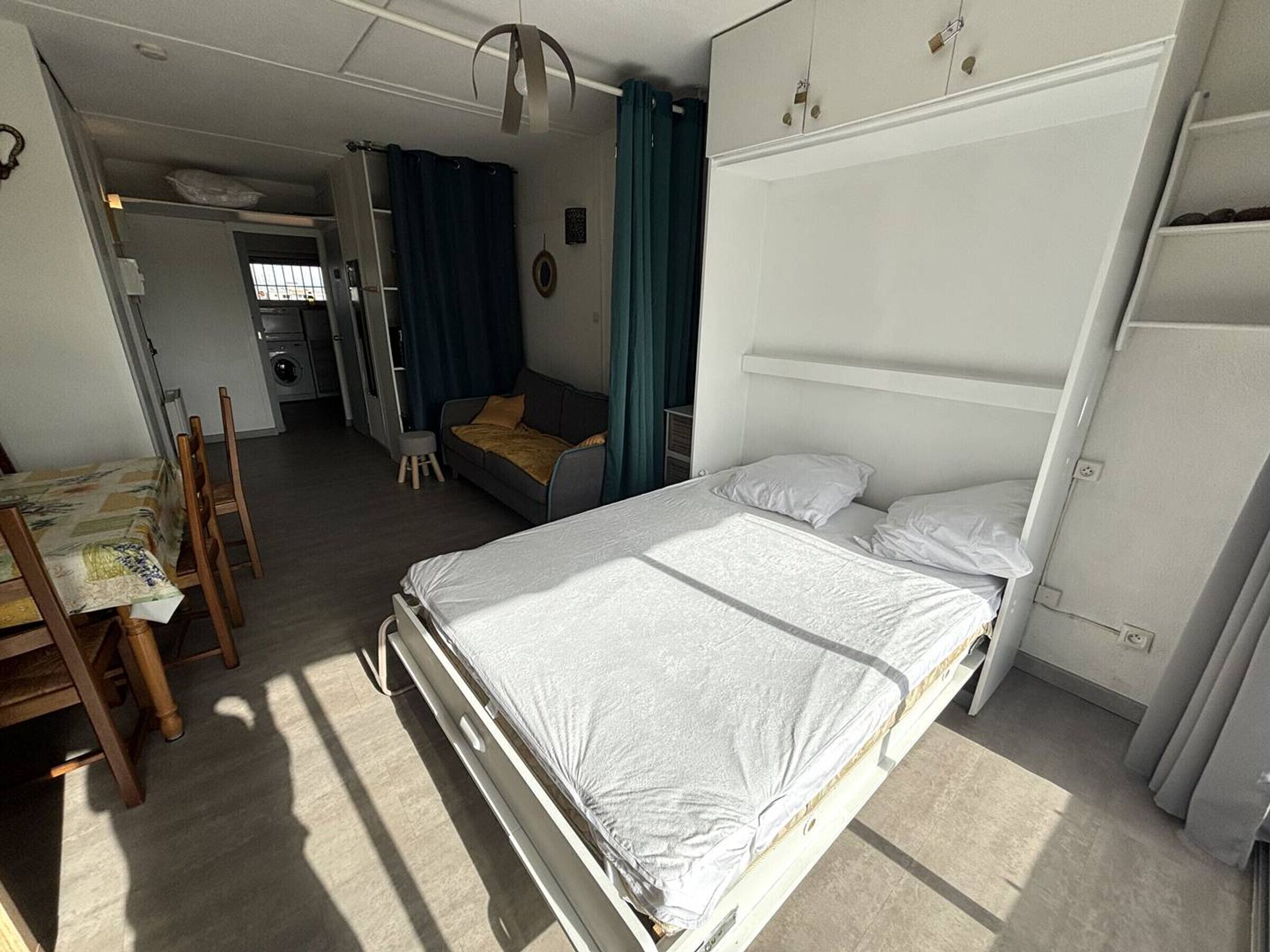 A compact room with a bed, a small table, and a sofa. There is a kitchenette in the background.