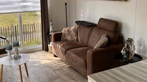 A living room with a brown sofa, a dining table, and a painting on the wall.