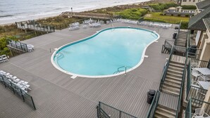 A swimming pool with a wooden deck, white lounge chairs, and a view of the beach and ocean. - Relax in Style Oceanview Villa w/ Resort Amenities & Steps to the Beach (Ocean Isle Beach)