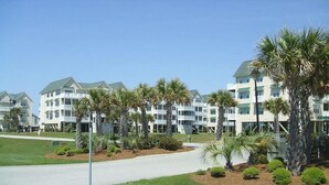 A row of multi-story buildings with balconies, surrounded by well-maintained lawns and palm trees. - Relax in Style Oceanview Villa w/ Resort Amenities & Steps to the Beach (Ocean Isle Beach)