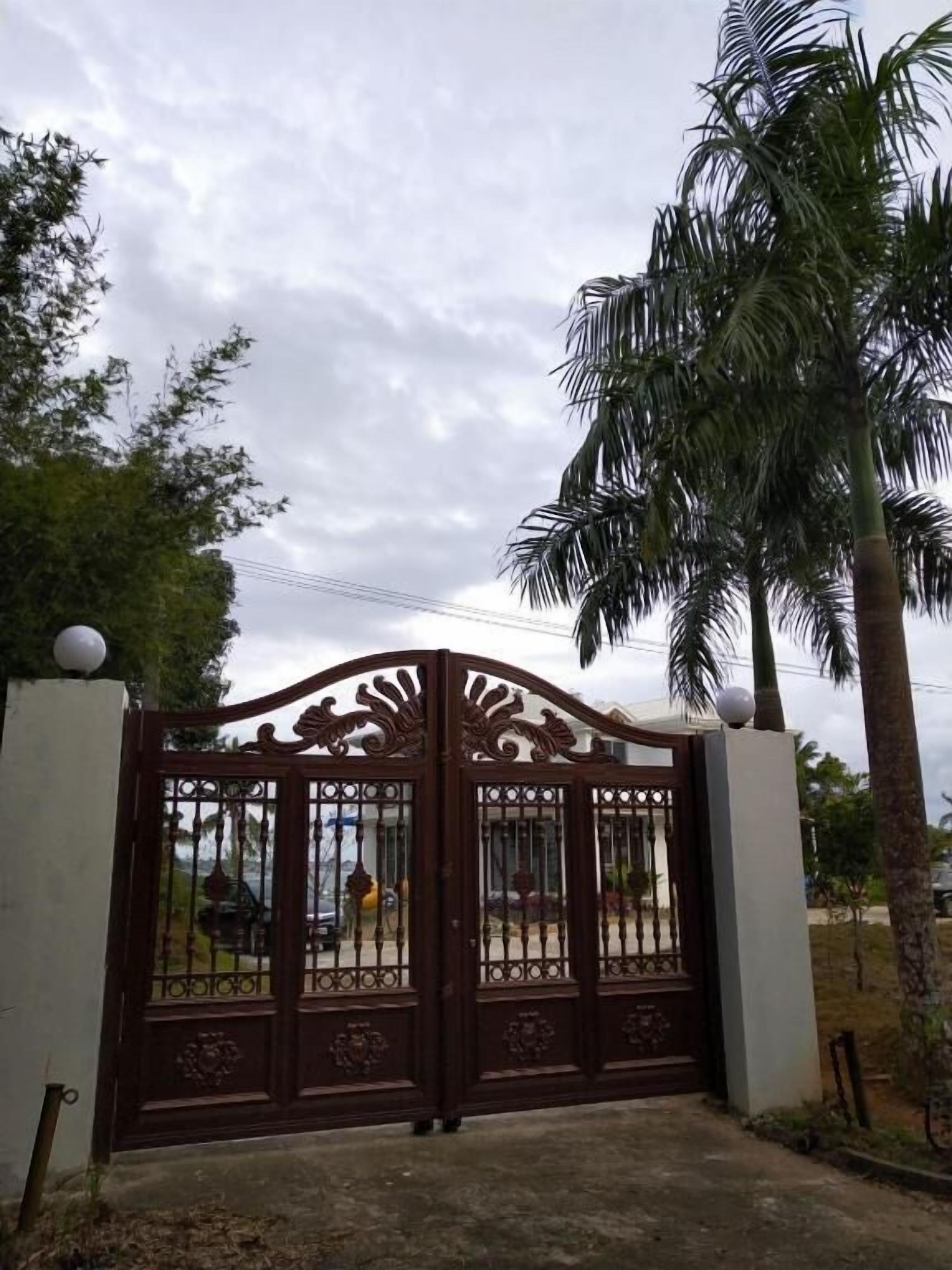 Una entrada cerrada con detalles ornamentales de metal, una palmera y un cielo nublado.