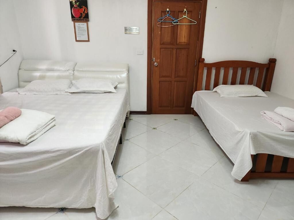 Een kamer met twee enkele bedden, een houten deur en een vloer van witte tegels.