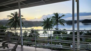 A covered balcony with a view of a lake and palm trees at sunset. - Suva Hideaway Villa (Suva)