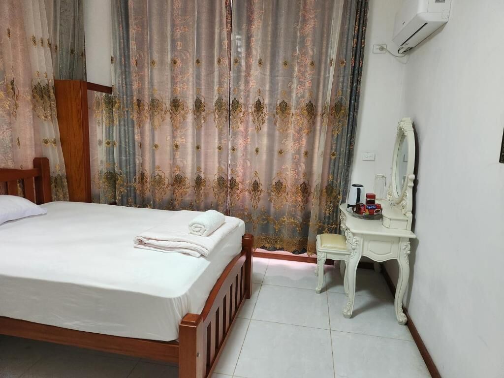 A bedroom with a wooden bed, a white bedside table, a mirror, and a curtain with a floral pattern.