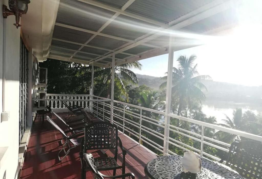 A covered balcony with a view of a body of water and palm trees.