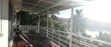 A covered balcony with a view of a body of water and palm trees.