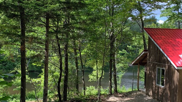 Una cabaña con techo rojo, rodeada de un bosque denso y un lago.