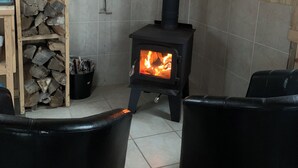 Una habitación acogedora con un hogar a leña, leña apilada y sillones de cuero negro.