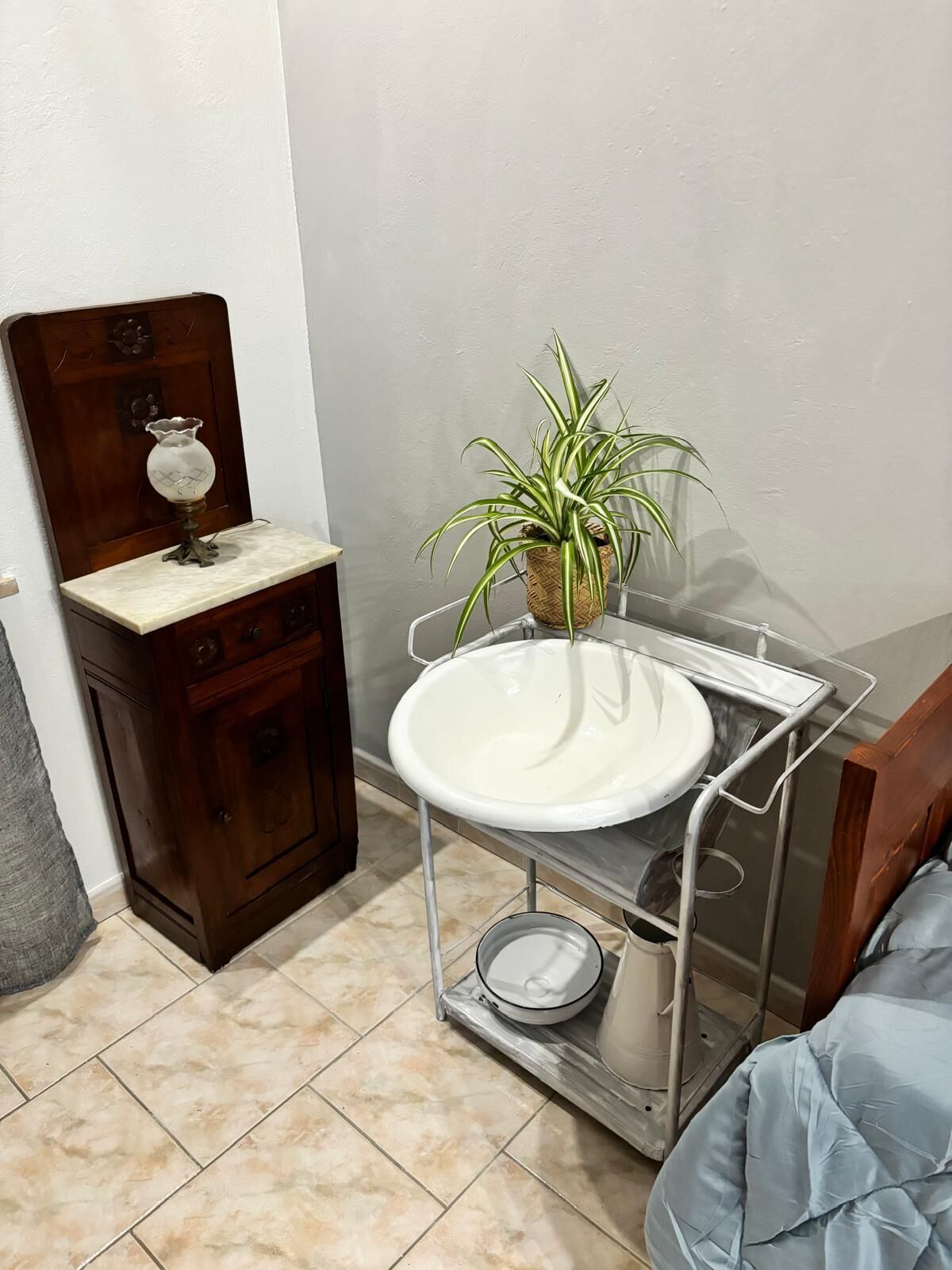 Un bagno con un armadietto in legno, un lavandino bianco su un supporto metallico, una pianta in vaso e un letto blu.