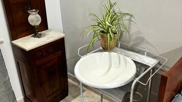 Un bagno con un armadietto in legno, un lavandino bianco su un supporto metallico, una pianta in vaso e un letto blu.