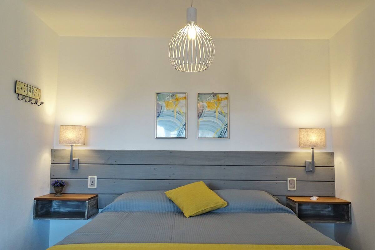 A bedroom with a bed, two bedside tables, a hanging light fixture, and two wall-mounted lamps.