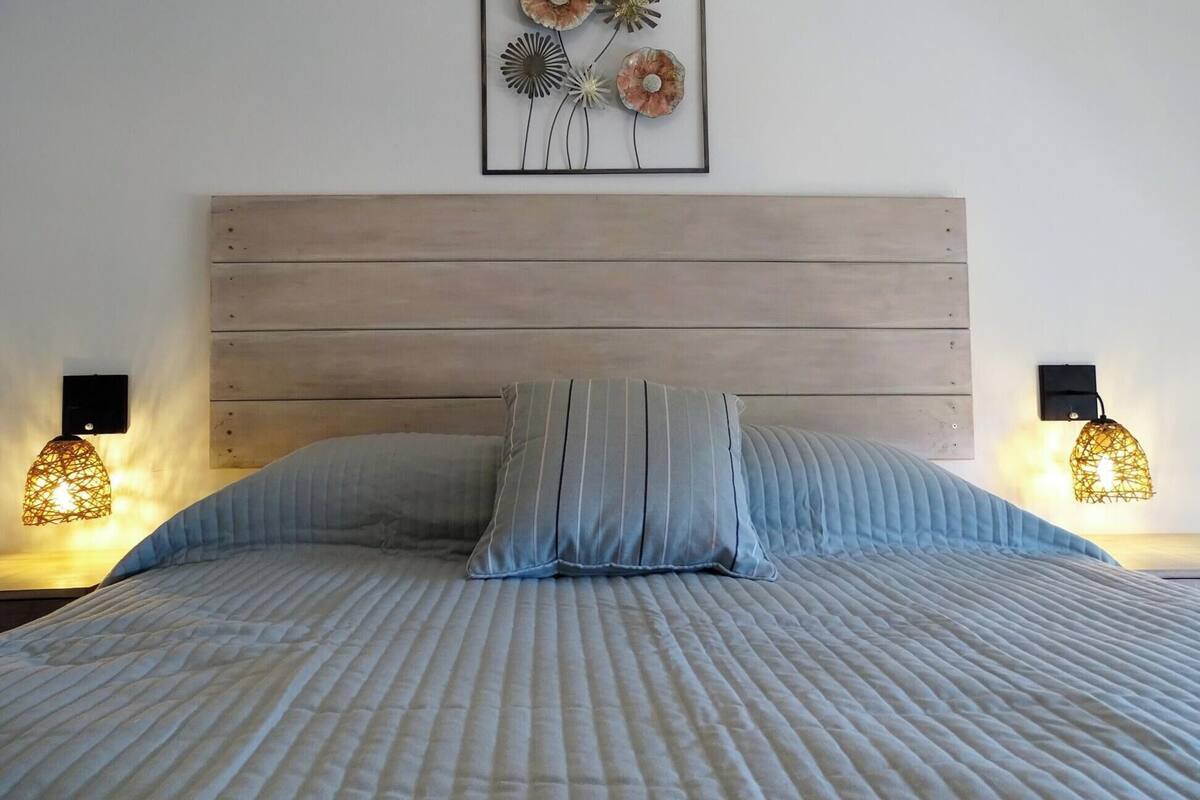 A neatly made bed with a striped pillow and a headboard. There are two wall-mounted lamps on either side of the bed.