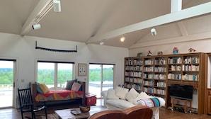 Ein geräumiges Wohnzimmer mit einer großen Bücherwand, einem Kamin und Blick ins Freie.