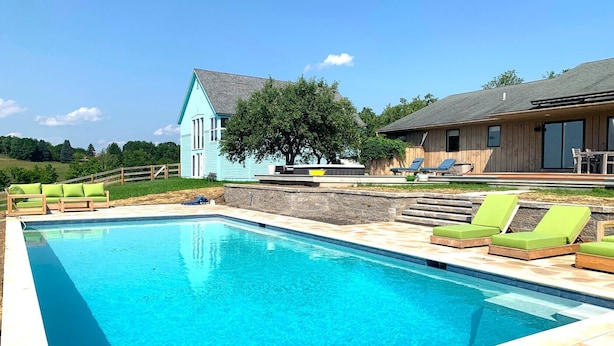 Ein Schwimmbad mit Liegestühlen, einer Holzterrasse und einem Haus mit blauer Fassade.