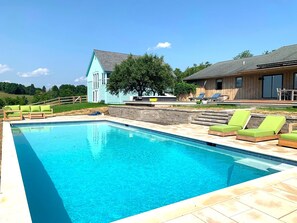 A swimming pool with lounge chairs, a wooden deck, and a house with a blue exterior. - Serene Farmhouse Villa: Pool + Hot Tub and Grill (Chatham)