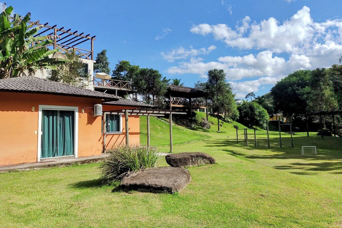 A house with a thatched roof, a wooden pergola, and a grassy yard with a soccer goal.