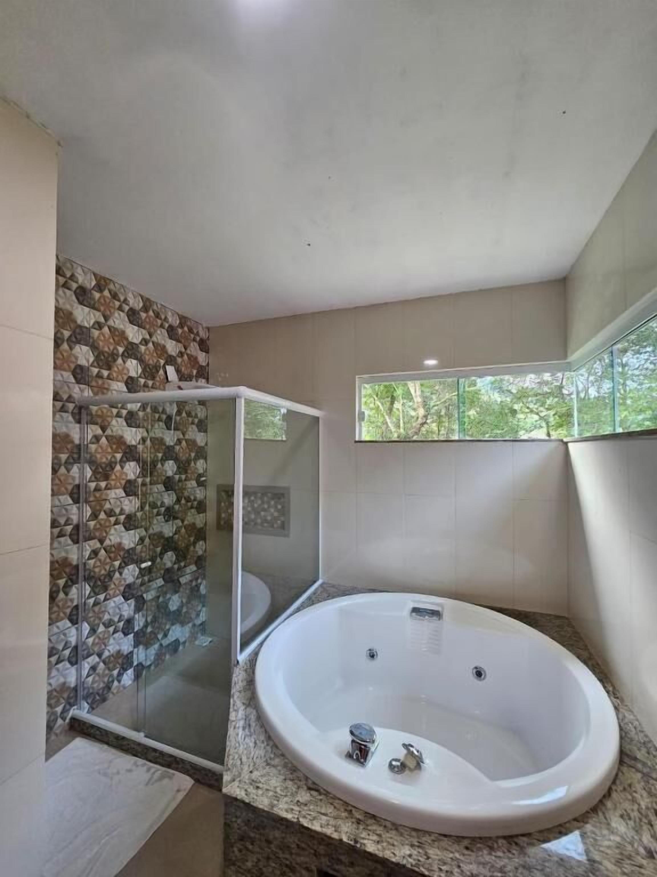 A modern bathroom with a freestanding bathtub, a glass shower enclosure, and a window providing a view of greenery.