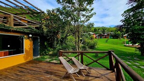 A wooden deck with two lounge chairs, surrounded by lush greenery and a well-maintained lawn.